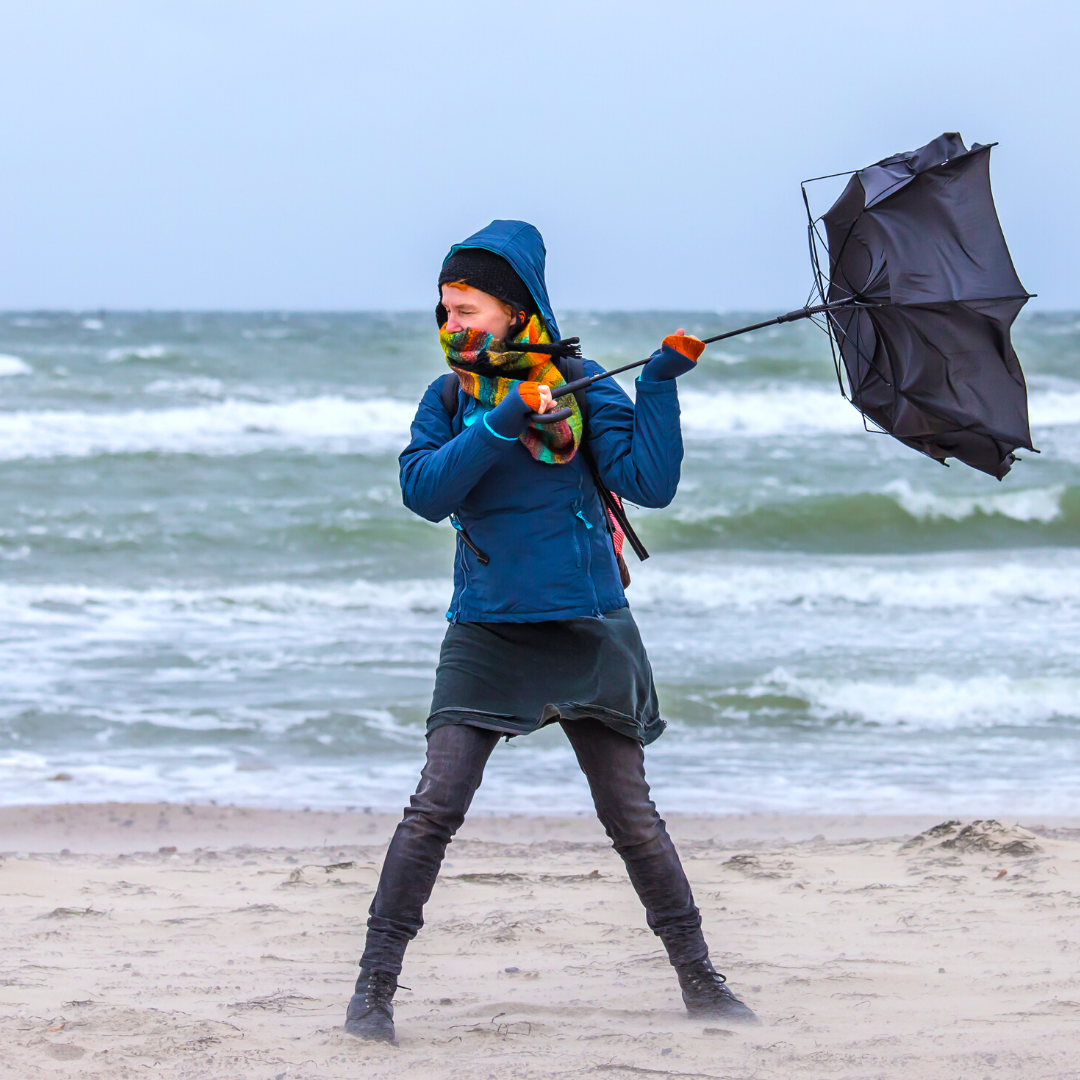 Woman at windy beach with broken umbrella